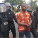 Liberian police escort ex-West Point Commissioner in handcuffs during CDC compound raid in Monrovia.