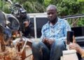 Arrested Radio BKS staff member seated near a motorcycle after being detained for allegedly carrying a locally made firearm in Nimba County on election day.