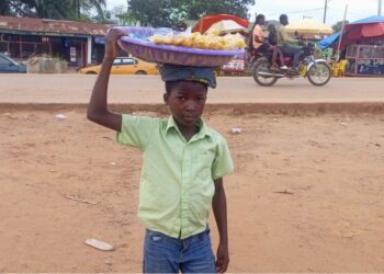 A young boy in Gbarnga, Bong County, carries a tray of snacks on his head while vending in the street instead of attending school.