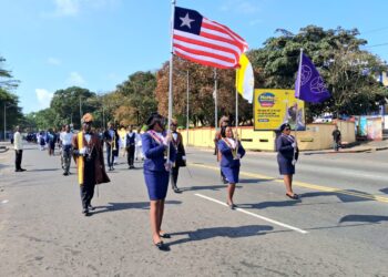 Ladies of Marshall members in ceremonial uniforms marching with the Liberian flag and organizational banner during a procession in Monrovia after Thanksgiving Mass.