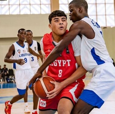 Liberian youth basketball player in white jersey defending an Egyptian opponent during a FIBA-sanctioned game.