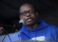 Acarous Gray in blue sweater speaking into a microphone