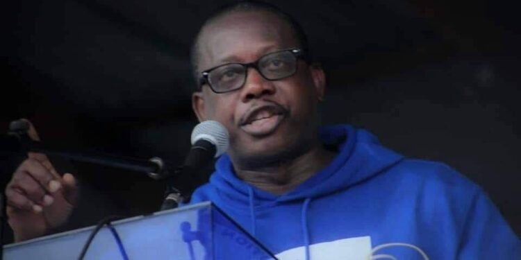 Acarous Gray in blue sweater speaking into a microphone