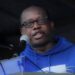 Acarous Gray in blue sweater speaking into a microphone
