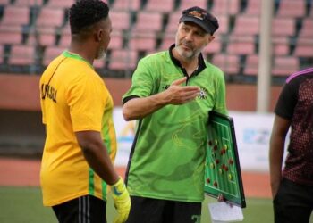 FC Fassell coach Amir Alagic strategizing with goalkeeper during a training session at the stadium, holding a tactics board while wearing the club’s green jersey.
