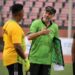 FC Fassell coach Amir Alagic strategizing with goalkeeper during a training session at the stadium, holding a tactics board while wearing the club’s green jersey.