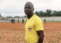 Liberian kickball referee Julius Suah standing on a dirt pitch during a local tournament in Nimba County before his arrest for alleged fuel theft