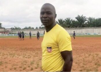Liberian kickball referee Julius Suah standing on a dirt pitch during a local tournament in Nimba County before his arrest for alleged fuel theft