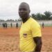 Liberian kickball referee Julius Suah standing on a dirt pitch during a local tournament in Nimba County before his arrest for alleged fuel theft