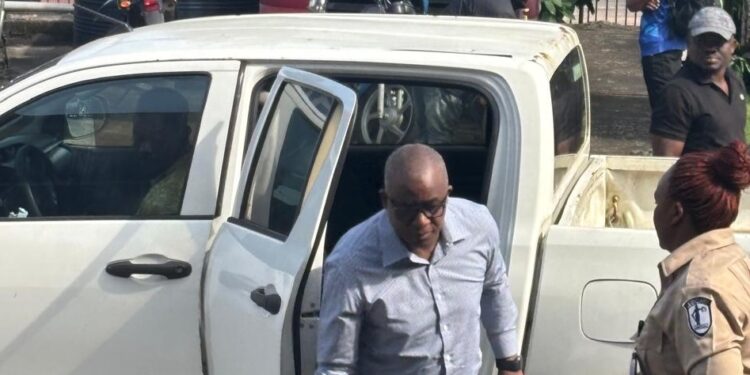 Former LTA chair Abdullai Kamara escorted by officers as he exits a prison transport vehicle after bond approval in Monrovia.