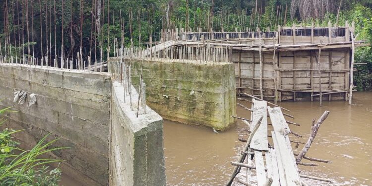 Unfinished bridge construction in Douta, Bong County, Liberia, where residents risk deadly creek crossings on a fragile wooden structure due to stalled works.
