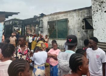 Residents gather outside a burned house on Caldwell Back Road in Monrovia after a late-night fire killed six people, including two children
