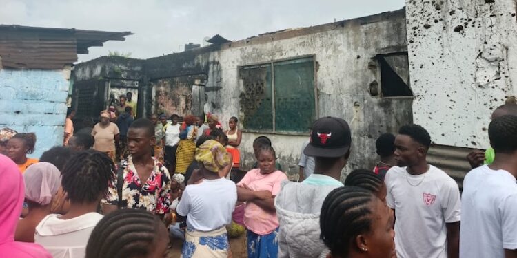 Residents gather outside a burned house on Caldwell Back Road in Monrovia after a late-night fire killed six people, including two children