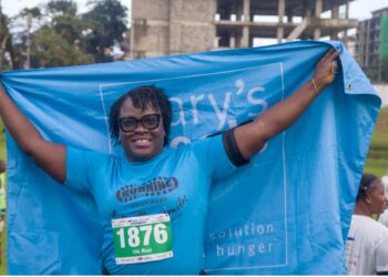 A Mary’s Meals runner celebrates at the Liberia Marathon finish line holding the organization’s blue banner, symbolizing hope and unity under the 3 Million Smiles campaign