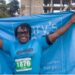 A Mary’s Meals runner celebrates at the Liberia Marathon finish line holding the organization’s blue banner, symbolizing hope and unity under the 3 Million Smiles campaign