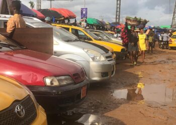 Commercial taxis line up at a busy Monrovia parking station as passengers walk by, highlighting drivers’ frustration over new fare cuts announced by the Transport Ministry