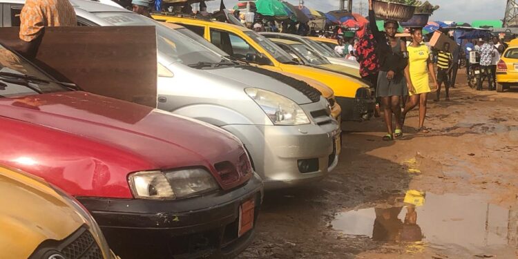 Commercial taxis line up at a busy Monrovia parking station as passengers walk by, highlighting drivers’ frustration over new fare cuts announced by the Transport Ministry