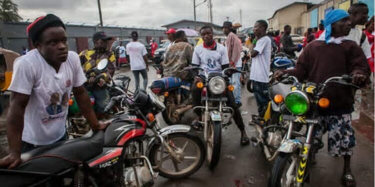 Young commercial motorbike riders in Gbarnga gather roadside, many forced to abandon higher education to earn a living through riding