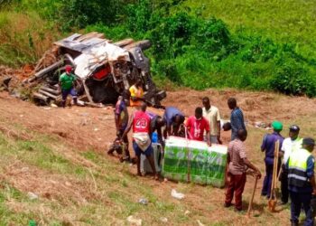 Police officers and residents recover goods and inspect a truck overturned in a fatal early-morning crash along Meleke Highway in Gbarnga, Bong County