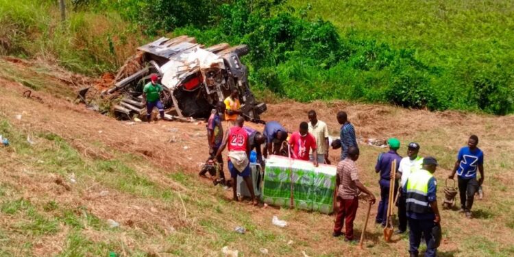 Police officers and residents recover goods and inspect a truck overturned in a fatal early-morning crash along Meleke Highway in Gbarnga, Bong County