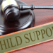 A wooden gavel beside a sign reading “Child Support,” symbolizing legal action against child support neglect in Grand Kru County, Liberia