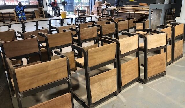 Rows of newly built wooden-and-metal classroom chairs at the Monrovia Vocational Training Center workshop, produced under the “One Chair, One Child” program funded by salaries withheld from suspended Liberian government officials