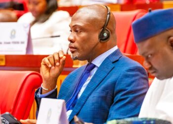 A man wearing a blue traditional outfit seated at a conference, identified as Representative Taa Wongbe of Nimba County District 9.