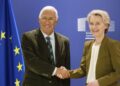 Two senior officials shaking hands in front of European Union flags during a diplomatic meeting