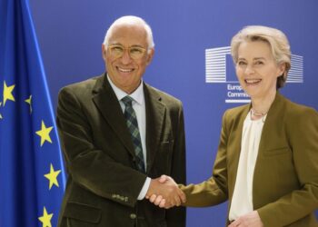 Two senior officials shaking hands in front of European Union flags during a diplomatic meeting