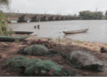 Fishing nets and canoes lying unused along the shore of the St. Paul River as sand mining boats operate in the distance