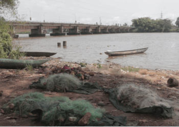 Fishing nets and canoes lying unused along the shore of the St. Paul River as sand mining boats operate in the distance
