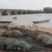 Fishing nets and canoes lying unused along the shore of the St. Paul River as sand mining boats operate in the distance