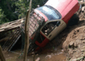 A pickup truck shown partially fallen or damaged on a deteriorated wooden bridge in a rural area, drawing attention to poor transportation infrastructure