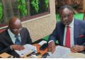 Two men seated at a table reviewing printed documents during a formal meeting, with folders, papers, and writing materials arranged on the table