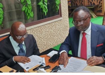 Two men seated at a table reviewing printed documents during a formal meeting, with folders, papers, and writing materials arranged on the table