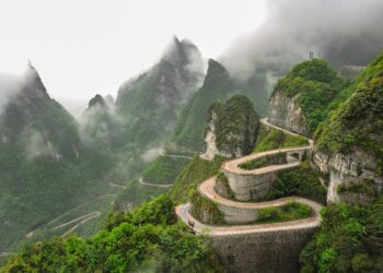 A winding mountain road in Zhangjiajie National Forest Park surrounded by lush green cliffs and misty peaks.
