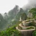 A winding mountain road in Zhangjiajie National Forest Park surrounded by lush green cliffs and misty peaks.