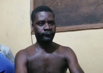 Emmanuel Gbayour seated shirtless during police questioning in Kakata, Liberia