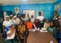 A group of community and civil society members seated and standing together in a meeting room during a press conference