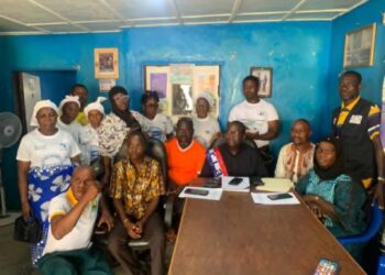 A group of community and civil society members seated and standing together in a meeting room during a press conference