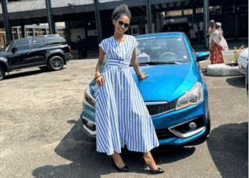 A woman standing beside a parked car in an outdoor area near a public building.