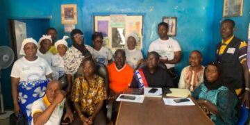 A group of community and civil society members seated and standing together in a meeting room during a press conference