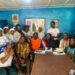 A group of community and civil society members seated and standing together in a meeting room during a press conference
