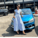 A woman standing beside a parked car in an outdoor area near a public building.