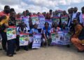 A group of students and community members holding public health awareness posters during an Mpox outreach campaign event