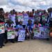 A group of students and community members holding public health awareness posters during an Mpox outreach campaign event
