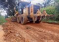 A road grader working on a dirt road in a rural community, leveling and clearing the surface for rehabilitation.