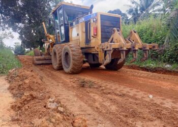 A road grader working on a dirt road in a rural community, leveling and clearing the surface for rehabilitation.