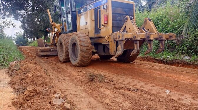 A road grader working on a dirt road in a rural community, leveling and clearing the surface for rehabilitation.