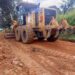 A road grader working on a dirt road in a rural community, leveling and clearing the surface for rehabilitation.